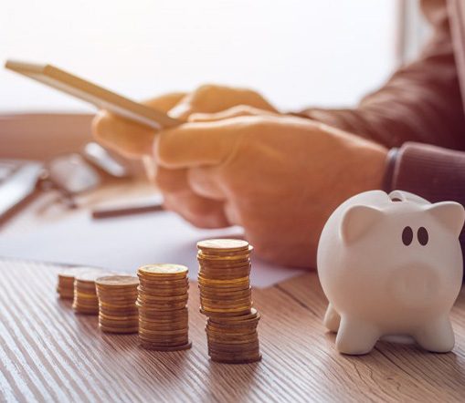 Man using a calculator at his desk while sitting next to his piggy bank