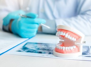 Gloved dentist’s hands at desk with pen, X-rays, paperwork, and model teeth
