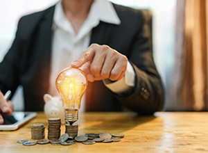 Man tapping a lightbulb that’s resting on top of a stack of coins