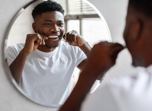 Patient smiling while flossing his teeth in bathroom