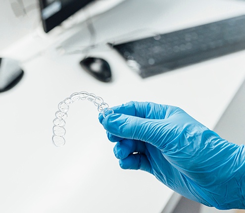 Dentist with blue glove holding clear aligner