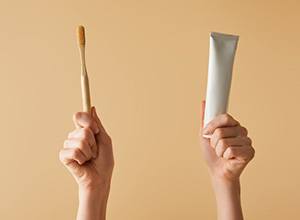 Two hands holding up a toothbrush and toothpaste