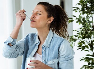 Woman smiling in content as she enjoys a spoonful of yogurt