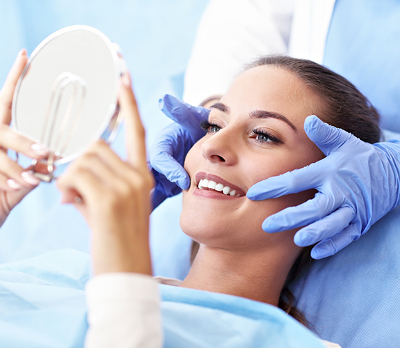 Woman sitting back in dental chair looking at smile in mirror