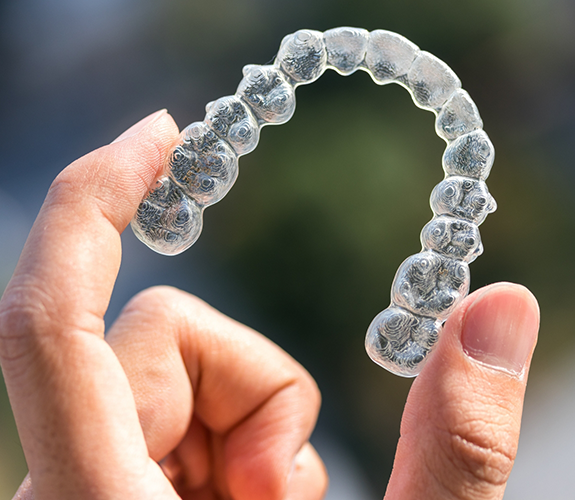 Close up of hand holding Invisalign clear aligner in West Palm Beach