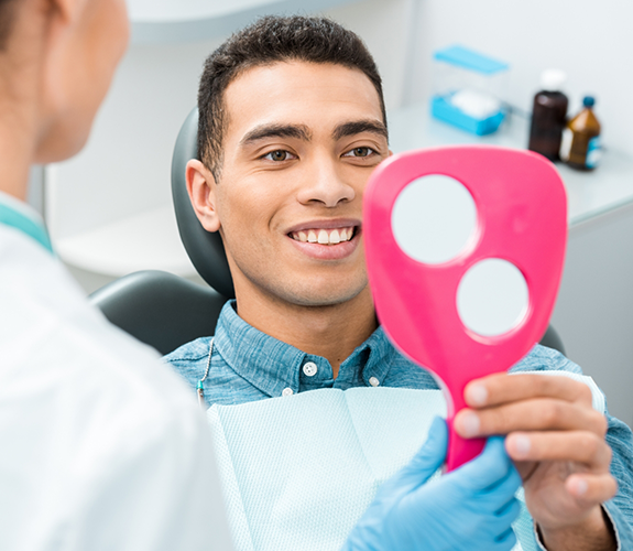 Man sitting in dental chair checking mirror