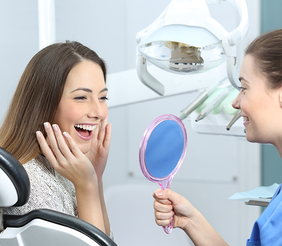 Dental patient smiling as team member shows them a mirror