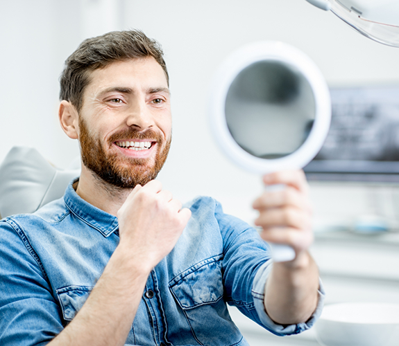 Man sitting in dental chair and checking smile in mirror