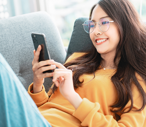 Woman with glasses lying on couch and looking at phone