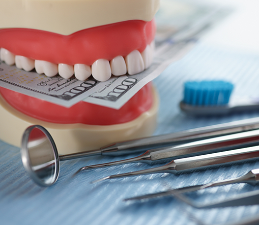 Dentures holding money sitting next to dental instruments