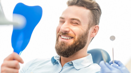 male-dental-patient-smiling-while-looking-at-himself-in-a-mirror